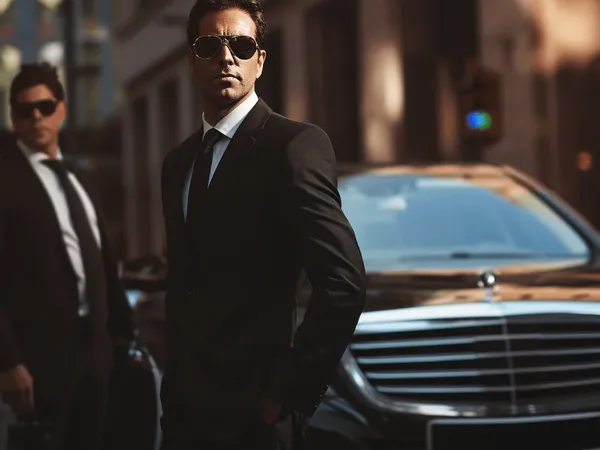 Chauffeurs in suits and sunglasses beside a black luxury sedan